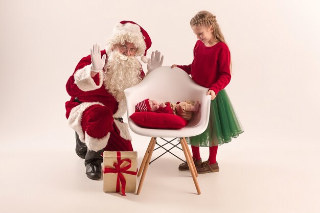 Retrato de Navidad de linda niña recién nacida y bonita hermana adolescente vestida con ropa de Navidad y hombre vestido con sombrero y traje de santa