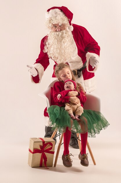 Retrato de Navidad de linda niña recién nacida y bonita hermana adolescente vestida con ropa de Navidad y hombre vestido con sombrero y traje de santa