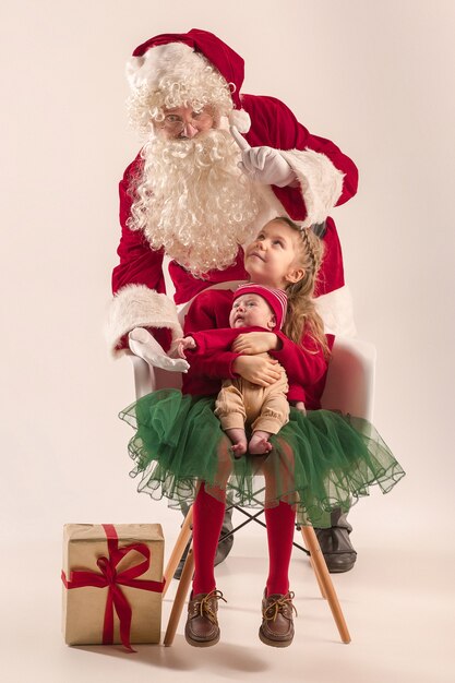 Retrato de Navidad de linda niña recién nacida y bonita hermana adolescente vestida con ropa de Navidad y hombre vestido con sombrero y traje de santa