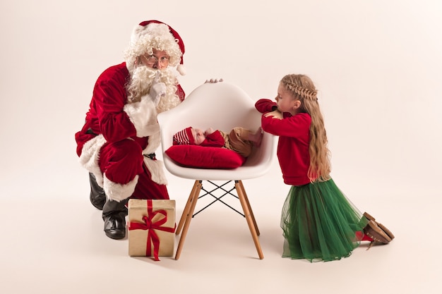 Retrato de Navidad de linda niña recién nacida, bonita hermana adolescente, vestida con ropa de Navidad y Santa Claus con caja de regalo