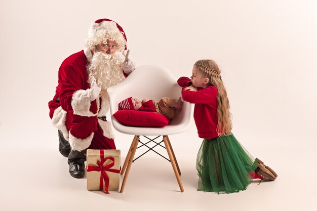 Retrato de Navidad de linda niña recién nacida, bonita hermana adolescente, vestida con ropa de Navidad y Santa Claus con caja de regalo