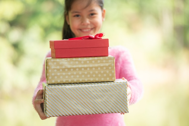 Retrato de Navidad de niña sonriente feliz con caja de regalo cerca de un árbol de rama verde. Bokeh de hojas verdes fuera de foco de fondo del bosque de la naturaleza.