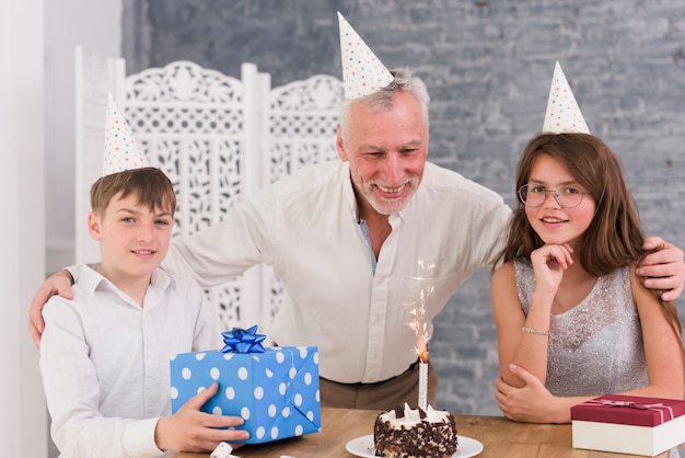 Retrato de nietos disfrutando de la fiesta de cumpleaños de su abuelo con pastel y cajas de regalo