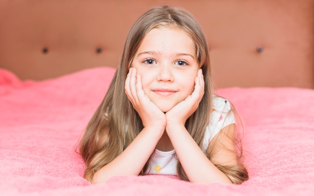 Retrato de una niña acostada en la sábana manta rosa en la cama