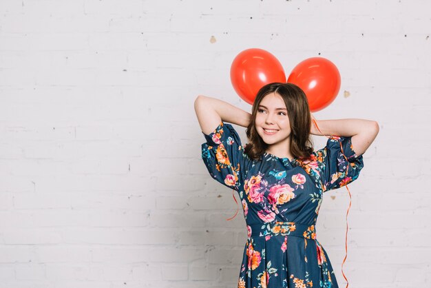 Retrato de niña adolescente sosteniendo globos rojos sobre su cabeza mirando lejos