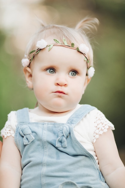 Retrato de niña adorable feliz en el parque con flores en la cabeza. Concepto de infancia feliz
