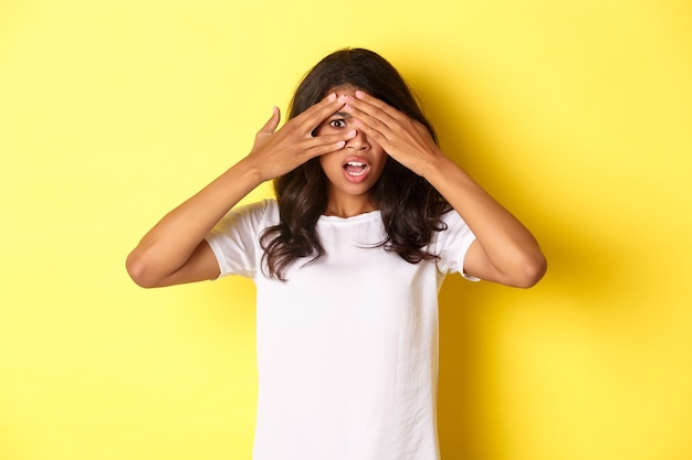 Foto gratuita retrato de niña afroamericana avergonzada y conmocionada cerró los ojos pero asomó a través de los dedos