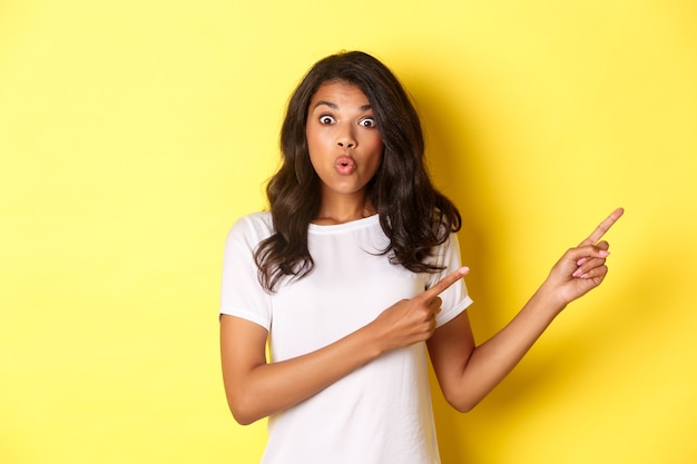 Retrato de niña afroamericana sorprendida e impresionada diciendo wow mirando asombrado mientras apunta