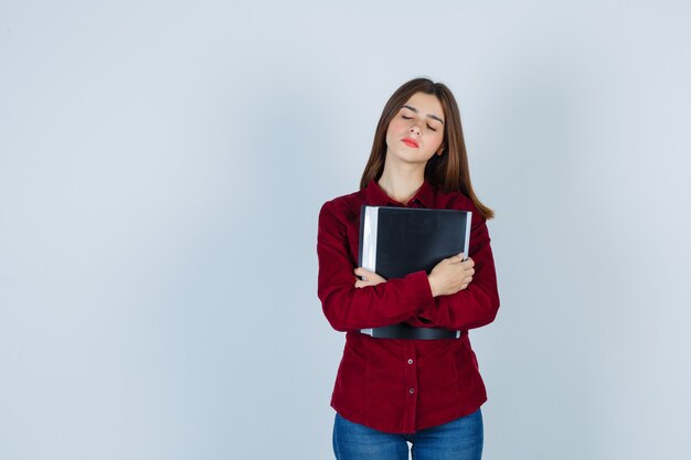 Retrato de niña agarrando la carpeta a su pecho, cerrando los ojos con camisa burdeos y mirando pensativo