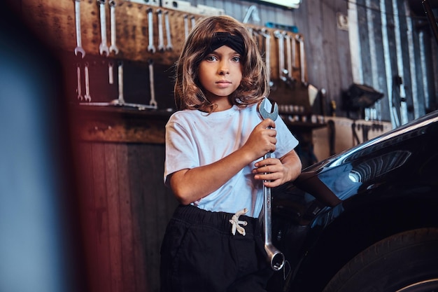 Retrato de una niña alegre con una gran llave en las manos cerca de un gar brillante en el servicio de automóviles.