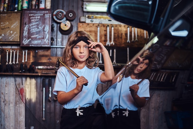 Retrato de una niña alegre con una gran llave en las manos cerca de un gar brillante en el servicio de automóviles.