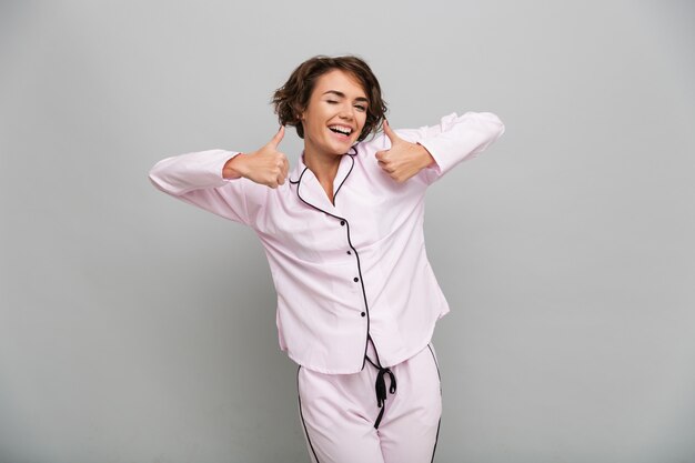 Retrato de una niña alegre en pijama mostrando los pulgares para arriba