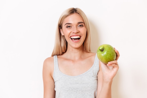 Retrato de una niña alegre en ropa interior mostrando manzana verde