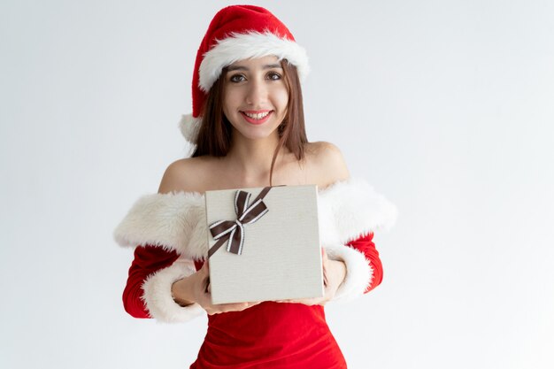 Retrato de niña alegre en vestido de santa claus dando caja de regalo