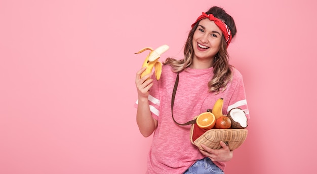 Retrato de una niña con alimentos saludables, frutas, en una pared rosa