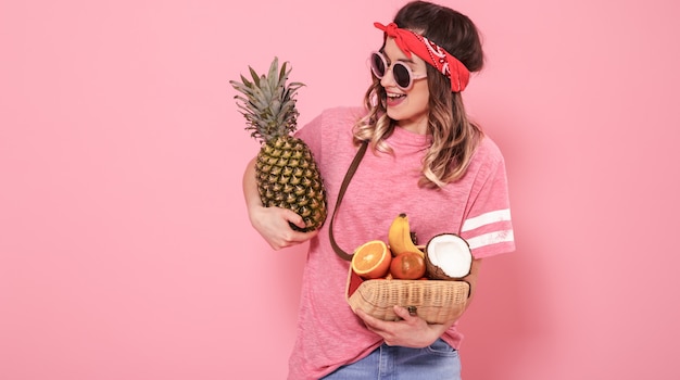 Foto gratuita retrato de una niña con alimentos saludables, frutas, en una pared rosa