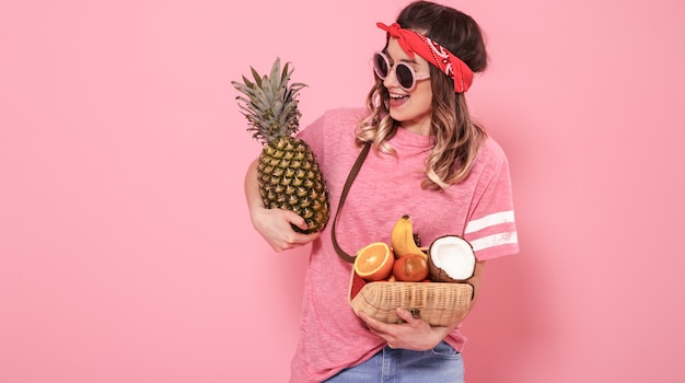 Retrato de una niña con alimentos saludables, frutas, en una pared rosa