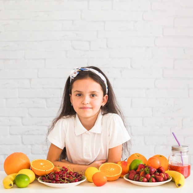 Retrato de una niña apoyándose en el escritorio con muchas frutas diferentes