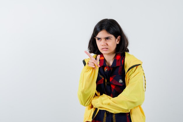 Retrato de niña apuntando a un lado en camisa a cuadros, chaqueta y mirando confiado vista frontal