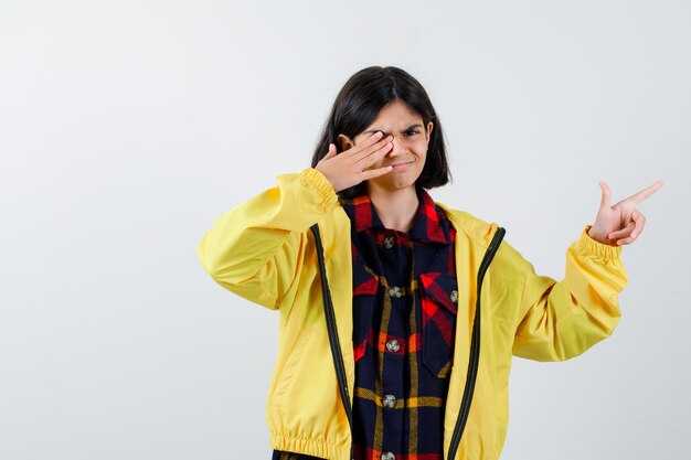 Retrato de niña apuntando hacia el lado derecho en camisa a cuadros, chaqueta y mirando confiado vista frontal