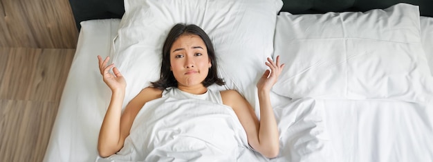 Foto gratuita el retrato de una niña asiática acostada en su cama y se encoge de hombros parece desconcertada pensando demasiado antes de irse a dormir