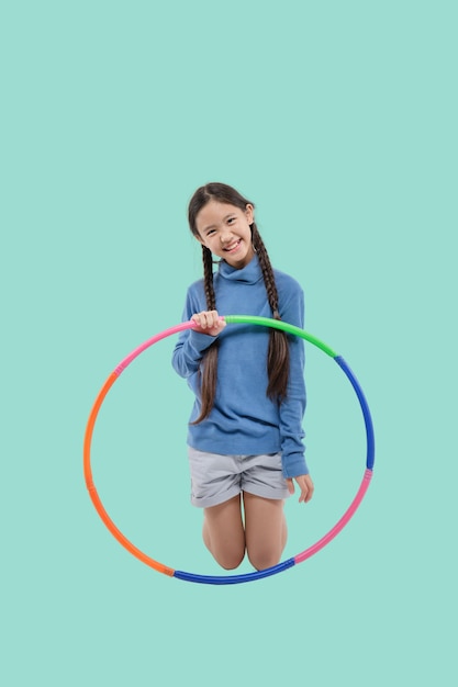 Retrato de una niña asiática feliz jugando hula hoop en un fondo verde  pastel aislado