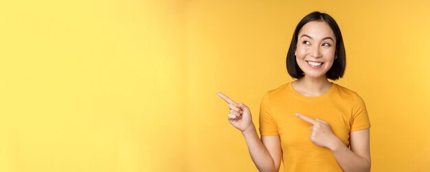 Retrato de niña asiática feliz señalando con el dedo y mirando a la izquierda sonriendo asombrada al ver la prohibición de promoción