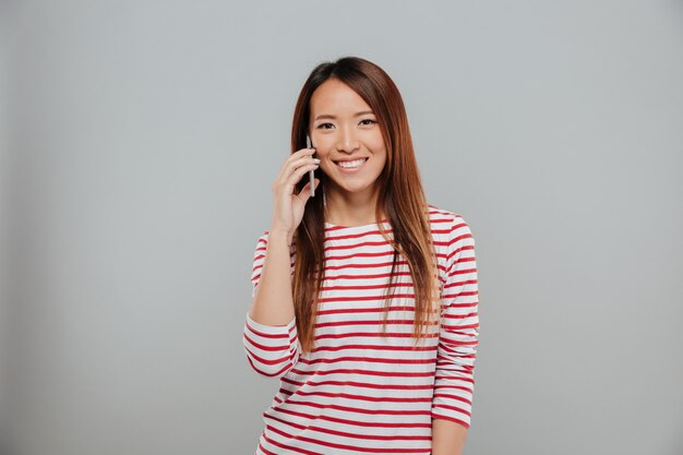 Retrato de una niña asiática sonriente hablando por teléfono móvil