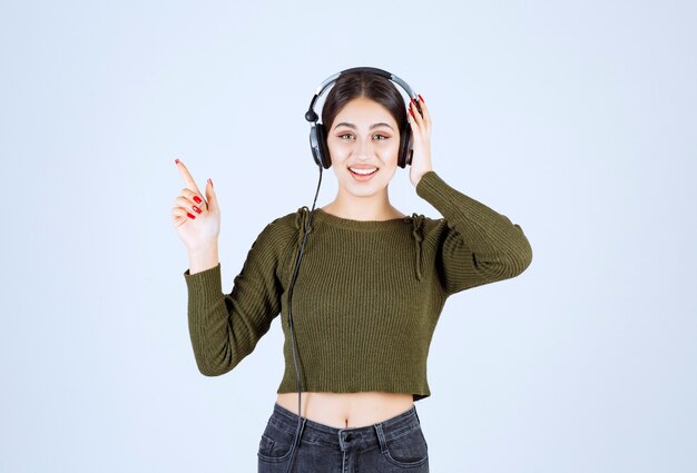 Retrato de niña en auriculares escuchando música y señalando.