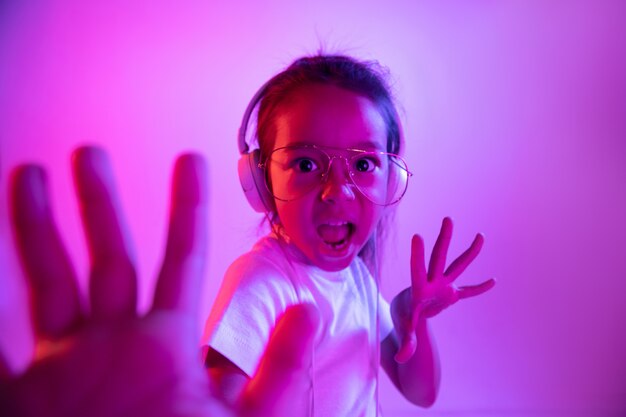 Retrato de niña en auriculares en pared degradado púrpura en luz de neón