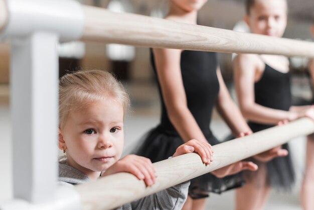 Retrato de niña con bailarines de pie cerca de la barra de madera