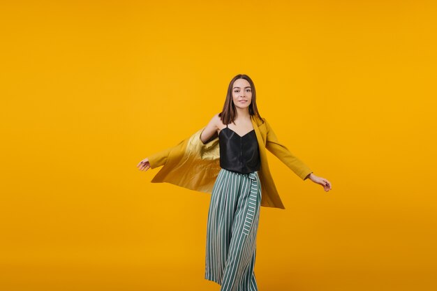 Retrato de niña blanca agradable bailando. Mujer alegre de pelo oscuro en pantalones a rayas divirtiéndose