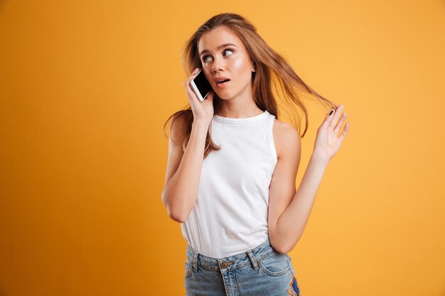 Retrato de una niña bonita perpleja hablando por teléfono móvil