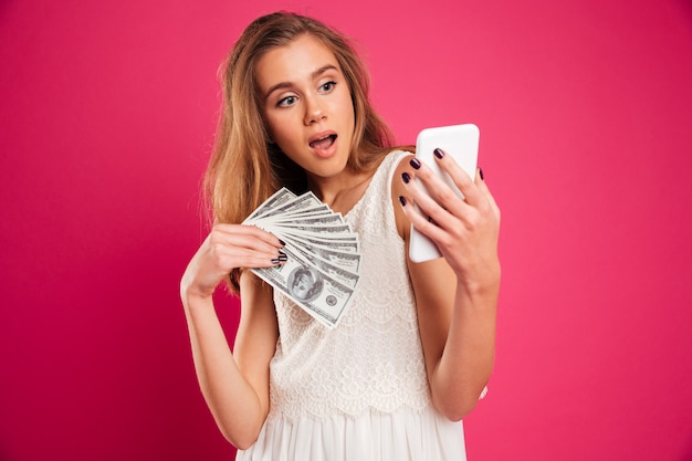 Retrato de una niña bonita sorprendida con billetes de dinero