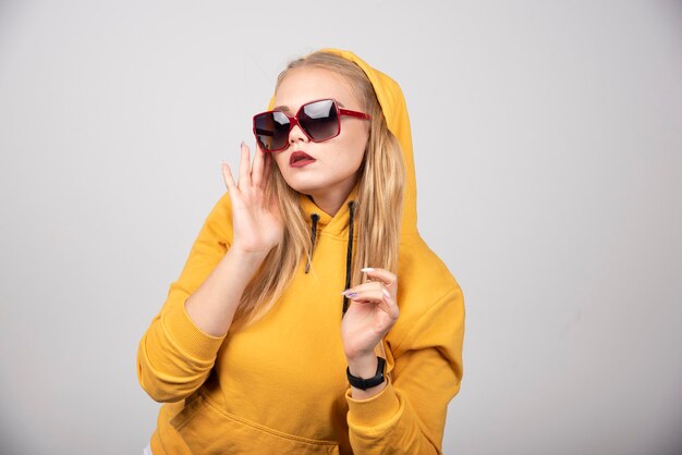 Retrato de niña bonita en sudadera con capucha amarilla con gafas elegantes.