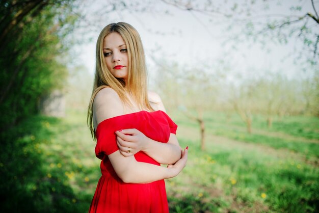 Retrato de niña de cabello claro en el jardín de primavera de fondo de vestido rojo