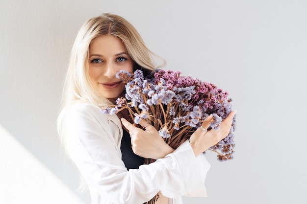 Retrato de niña con camisa blanca, sosteniendo un gran ramo de flores secas en gris