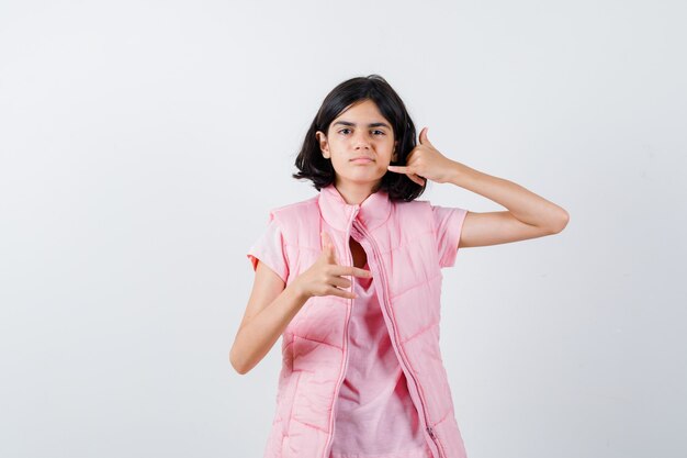 Retrato de una niña en camiseta blanca y chaleco acolchado mostrando gesto de teléfono