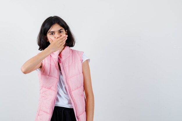 Retrato de una niña en camiseta blanca y chaleco hinchable que cubre la boca