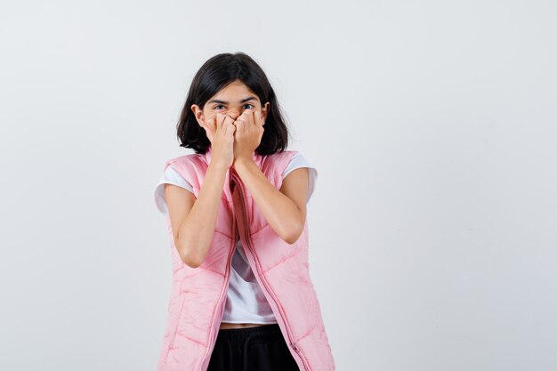 Retrato de una niña en camiseta blanca y chaleco hinchable que cubre su boca