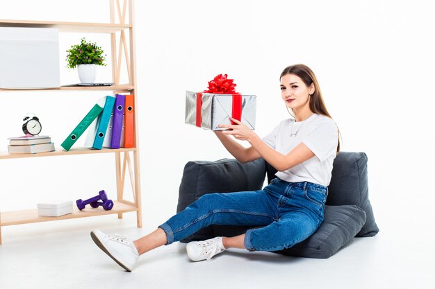 Retrato de una niña casual sentado en un piso con una pila de cajas de regalo y mirando a otro lado aislado sobre la pared blanca