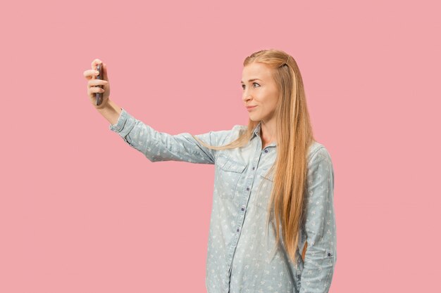 Retrato de una niña casual sonriente feliz que muestra el teléfono móvil de la pantalla en blanco aislado sobre la pared rosada