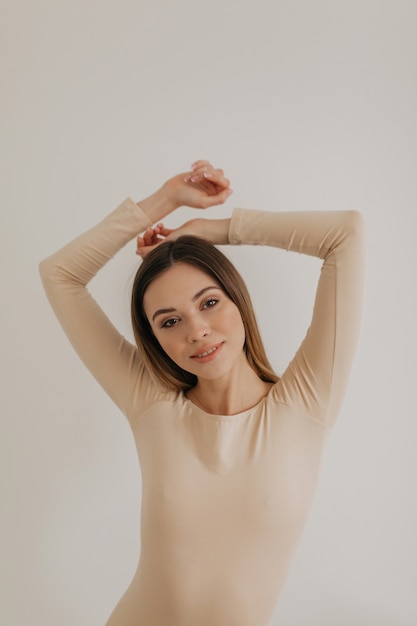 Foto gratuita retrato de niña caucásica con maquillaje natural y cabello rubio posando sobre una pared blanca con las manos levantadas.