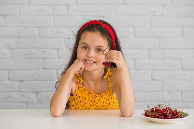 Retrato de una niña con cerezas rojas en un plato