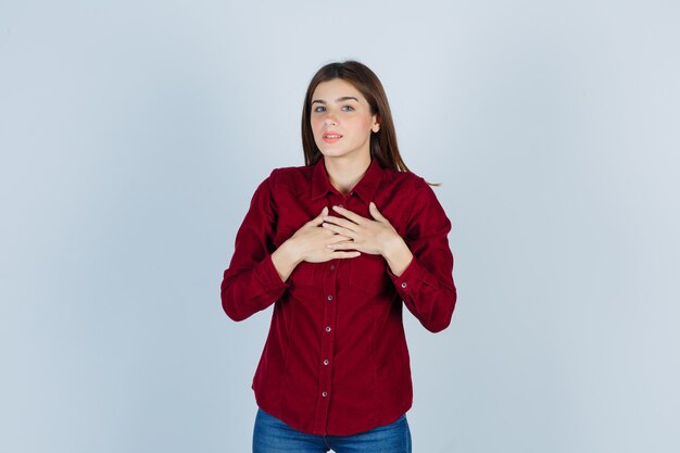 Retrato de niña cogidos de la mano en el pecho en camisa casual y mirando avergonzado