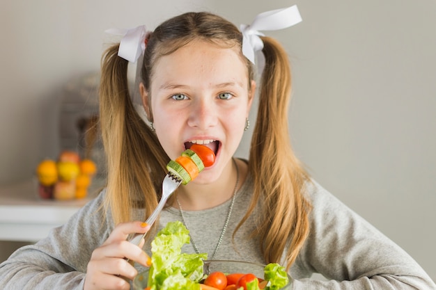 Retrato de una niña comiendo ensalada de vegetales frescos con tenedor