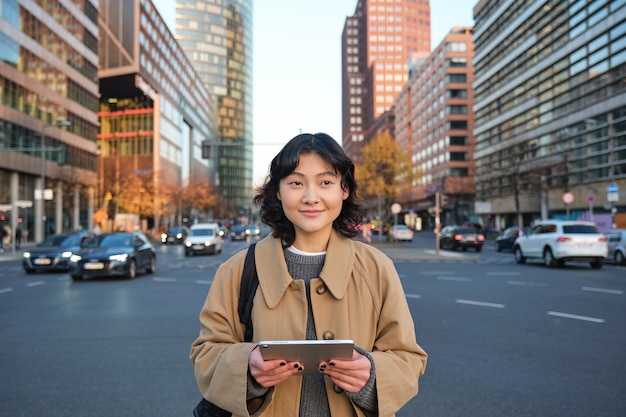 Foto gratuita retrato de niña coreana sonriente se encuentra en la concurrida calle del centro de la ciudad tiene rel informal de tableta digital