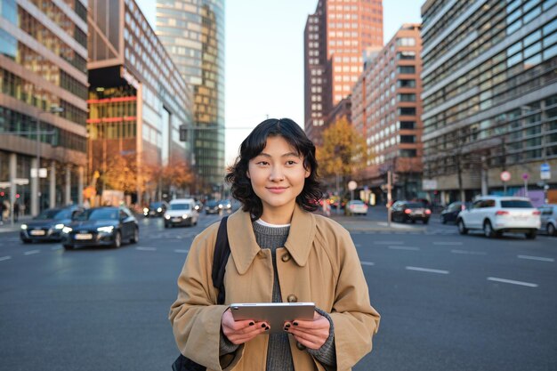 Retrato de niña coreana sonriente se encuentra en la concurrida calle del centro de la ciudad tiene rel informal de tableta digital