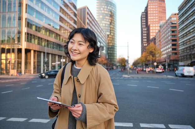 Retrato de niña coreana sonriente se encuentra en la concurrida calle del centro de la ciudad tiene rel informal de tableta digital