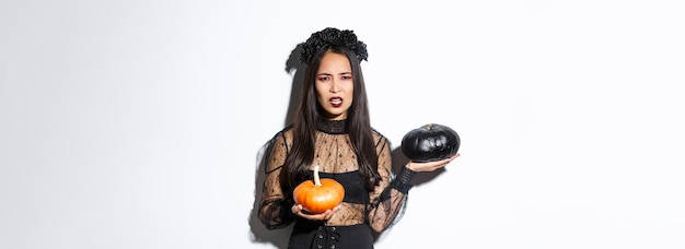 Foto gratuita retrato de niña decepcionada con el ceño fruncido en traje de bruja sosteniendo calabazas y quejándose de hacer muecas w